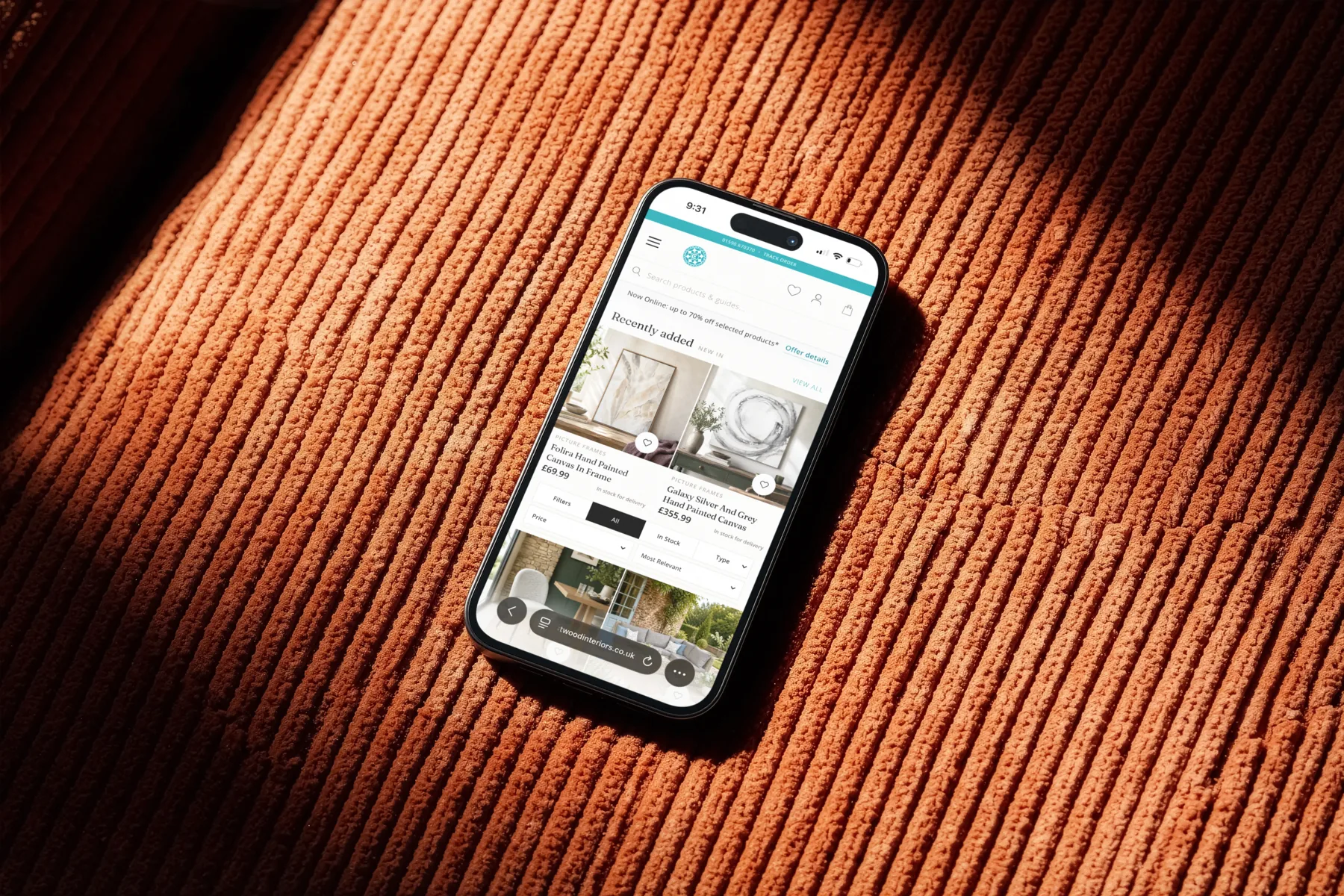 Phone on terracotta corduroy showing Crestwood Interiors Recently added product cards with square images, prices, and stock status